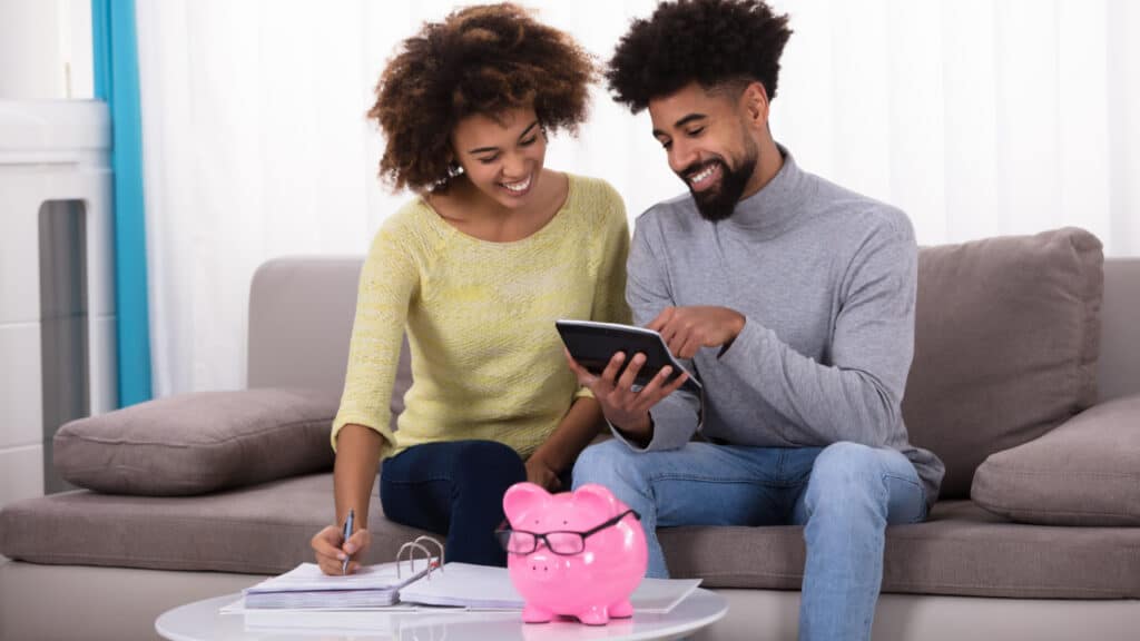 Smiling Young Couple Sitting On Sofa Calculating Budget