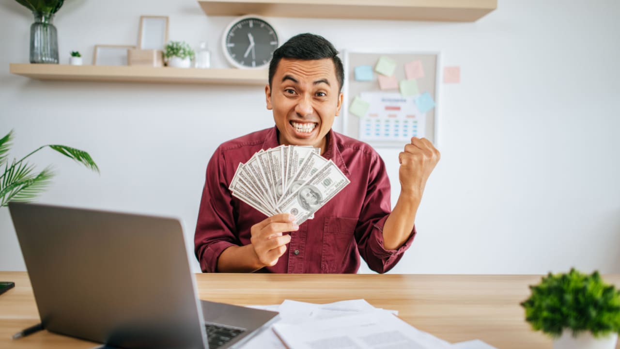 excited man with cash in home office