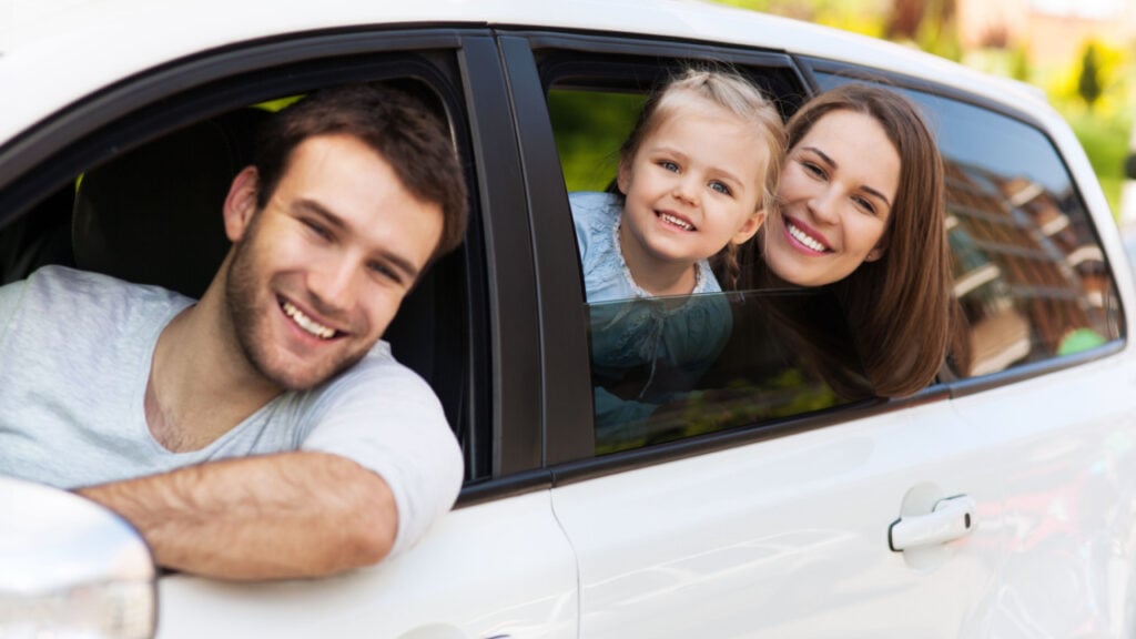 Happy family in white vehicle. Husband, wife, and child. Car is insured and they are happy.
