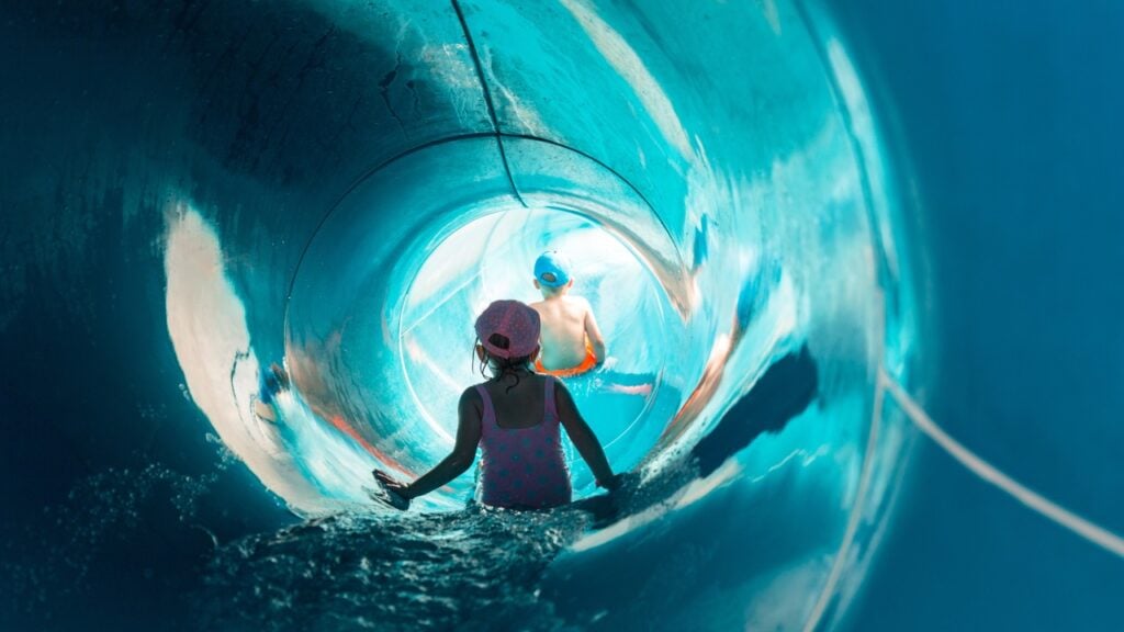 Two kids sliding down a blue waterslide.