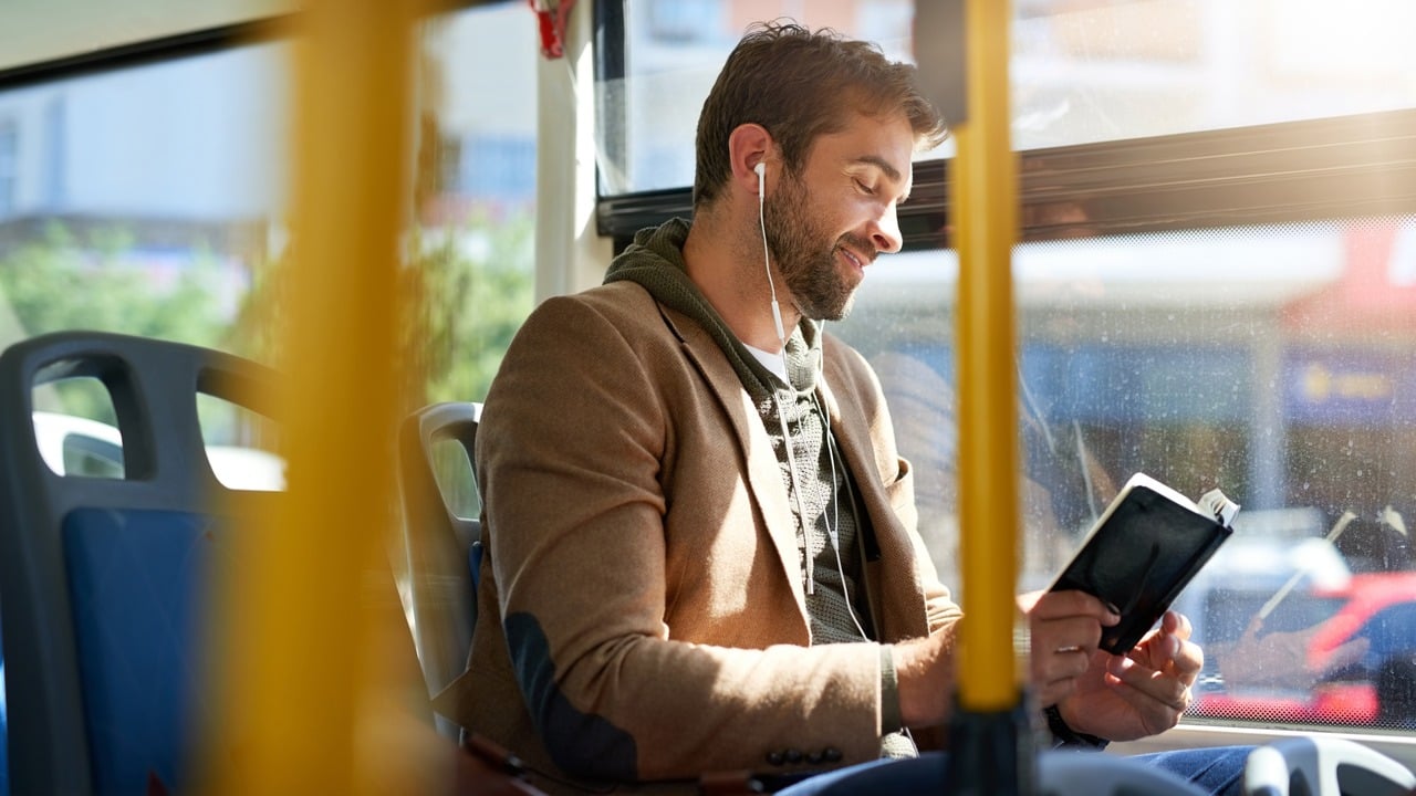A younger man reading on a bus on a sunny day.