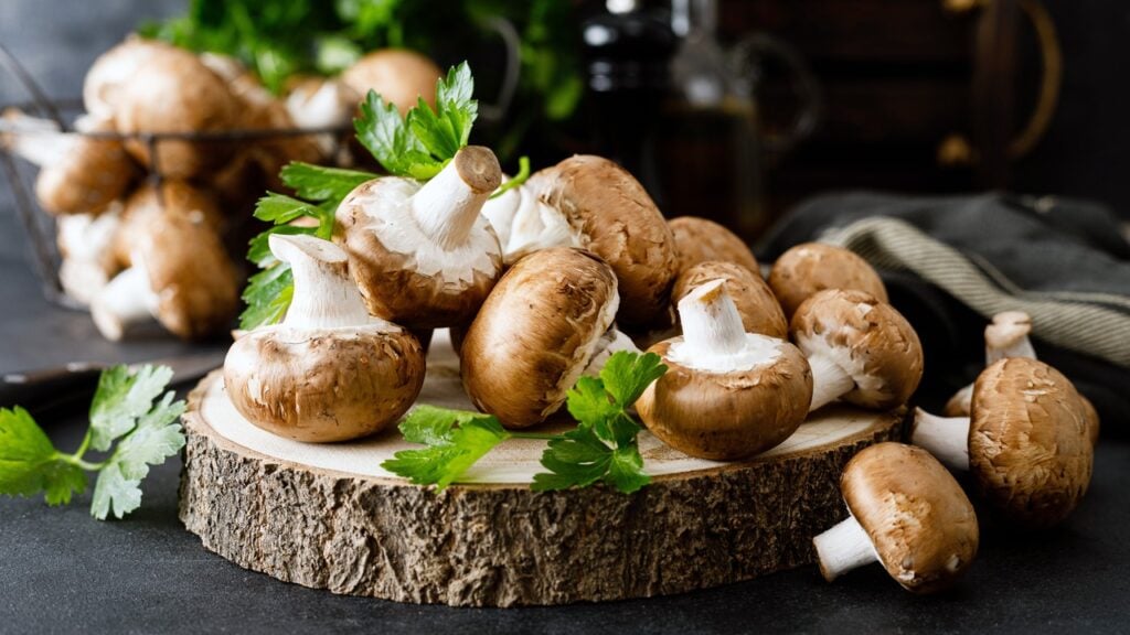 A group of button mushrooms on a wooden plate.