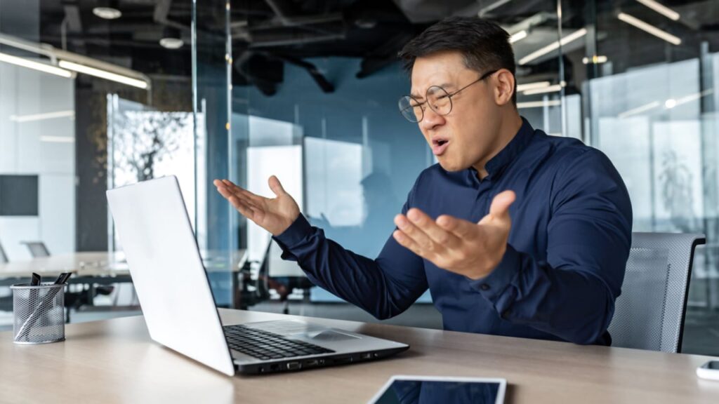 Dissatisfied and confused in depression asian financier investor, male businessman working dissatisfied with exchange rate, broker in despair Frustrated and angry asian boss yelling at laptop, failure man working inside twisted office building at desk