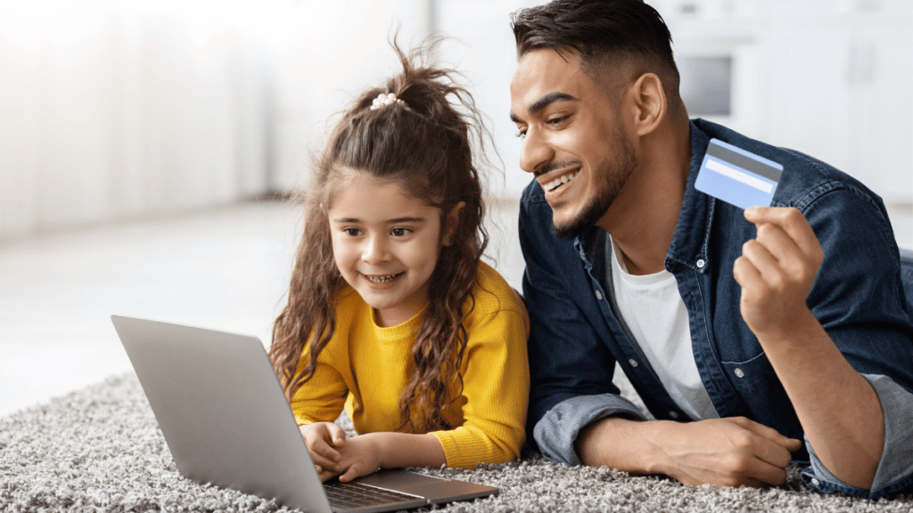 Father and child laying on the floor with a debit card and laptop
